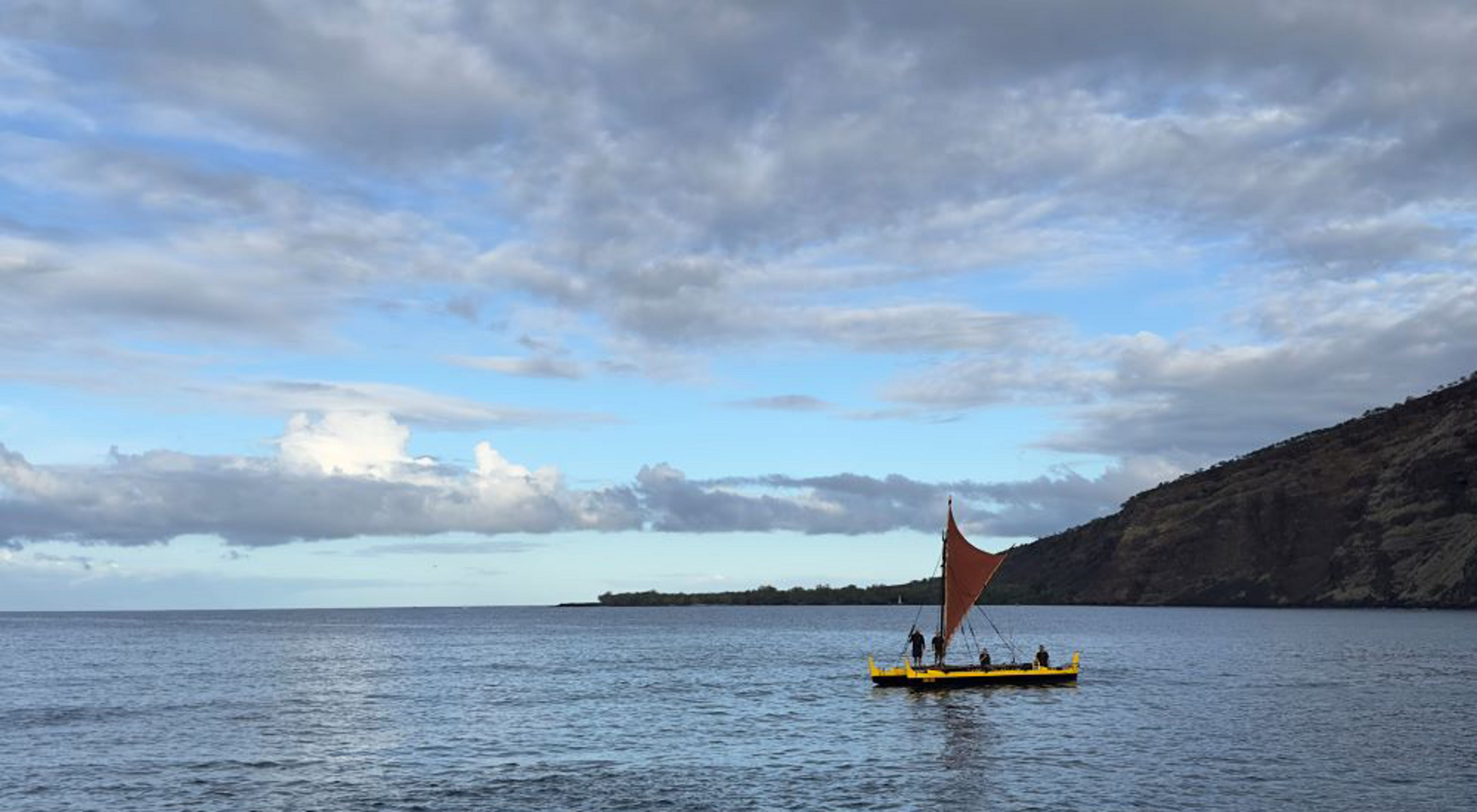 A bay in Hawai'i with two boats headed back in to shore with a green mountain rising in the background.