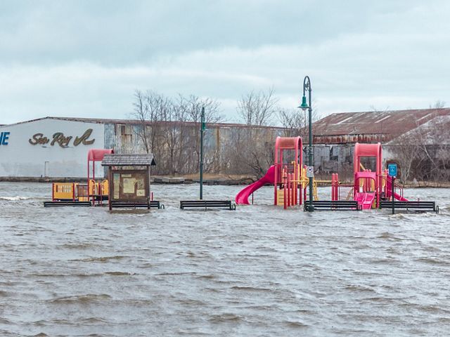 A playground flooded with one to two feet of water at Tennean Beach in Dorchester, with warehouses in the background.