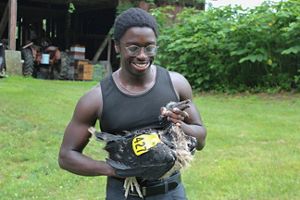 A person with glasses and black tank top smiles holding a bird with a tag on it.
