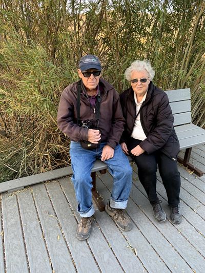 Two people sitting on a bench with trees behind them.