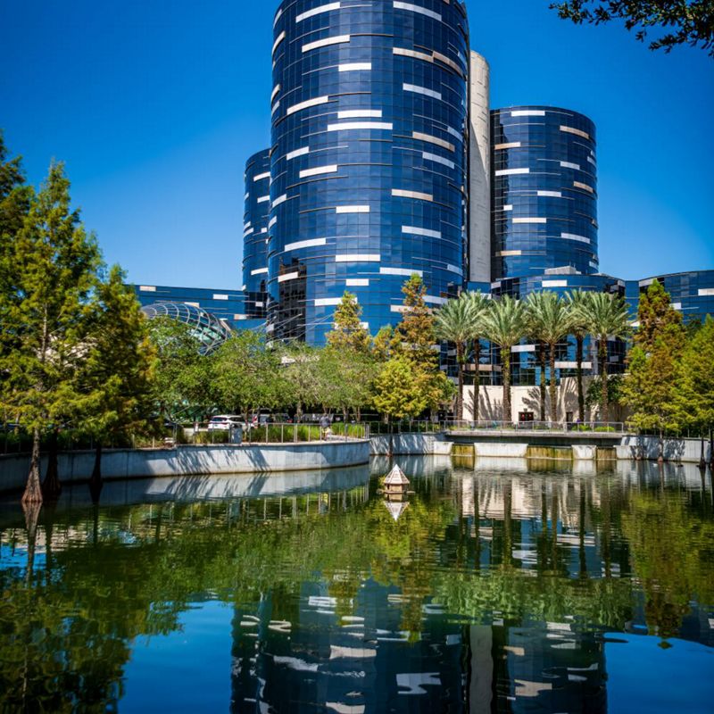 Skyline with black cylinder like buildings and lower tree line reflecting on a lake.