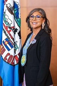 A headshot of a Native American woman with glasses smiling at the camera being sworn into a government position.