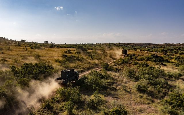 two large trucks driving through an African savannah.