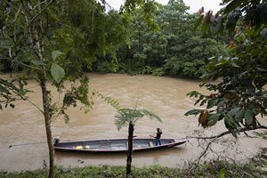 Un hombre se encuentra en una canoa larga y estrecha con motor en el río Curaray, que es marrón por la lluvia, con una densa selva tropical en ambas orillas.