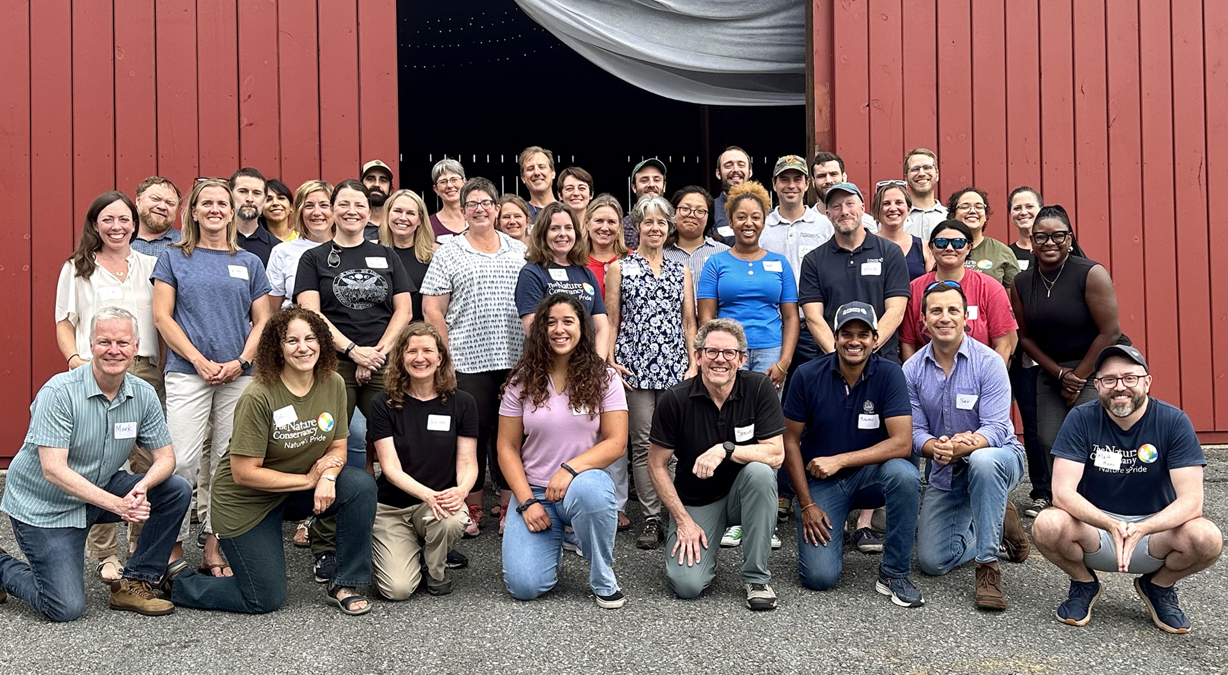 Group photo of TNC MD/DC staff. A large group of people stand together outdoors in front of a red barn, smiling during the chapter's annual staff retreat.
