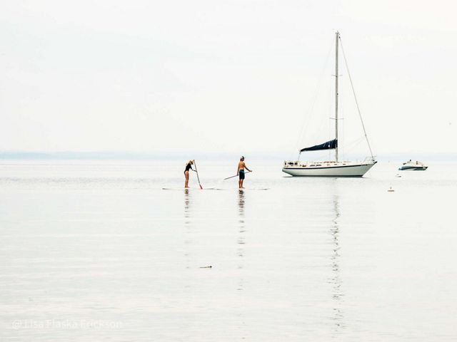 Two people paddleboard on Old Mission Peninsula with sailboats nearby. 