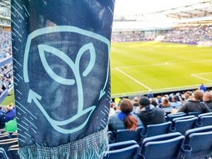 A scarf with the Sporting Sustainability logo being held with the soccer field in the background.