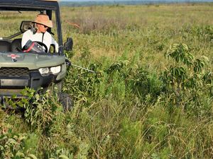 A man sits in a UTV on an open prairie spraying invasive plants.