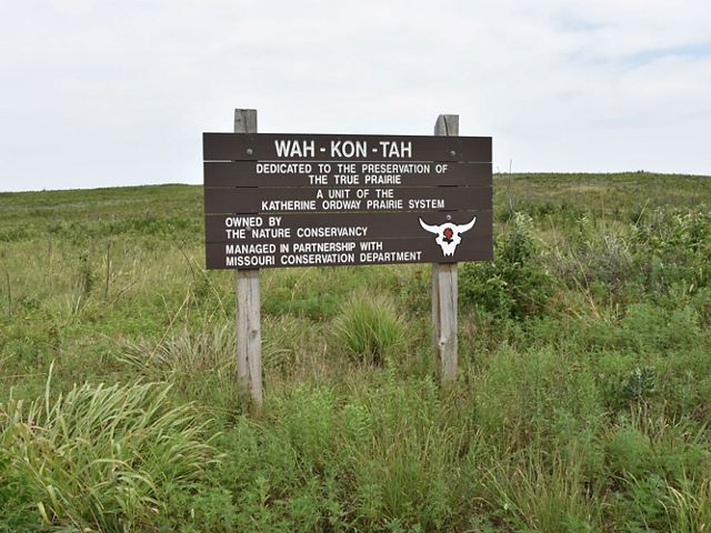 A wooden sign with preserve name 'Wah-Kon-Tah' on it sits in an open prairie field.