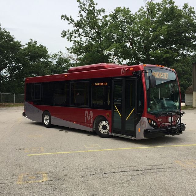 A red city bus parked in a parking lot with "Manchester" on the destination sign.