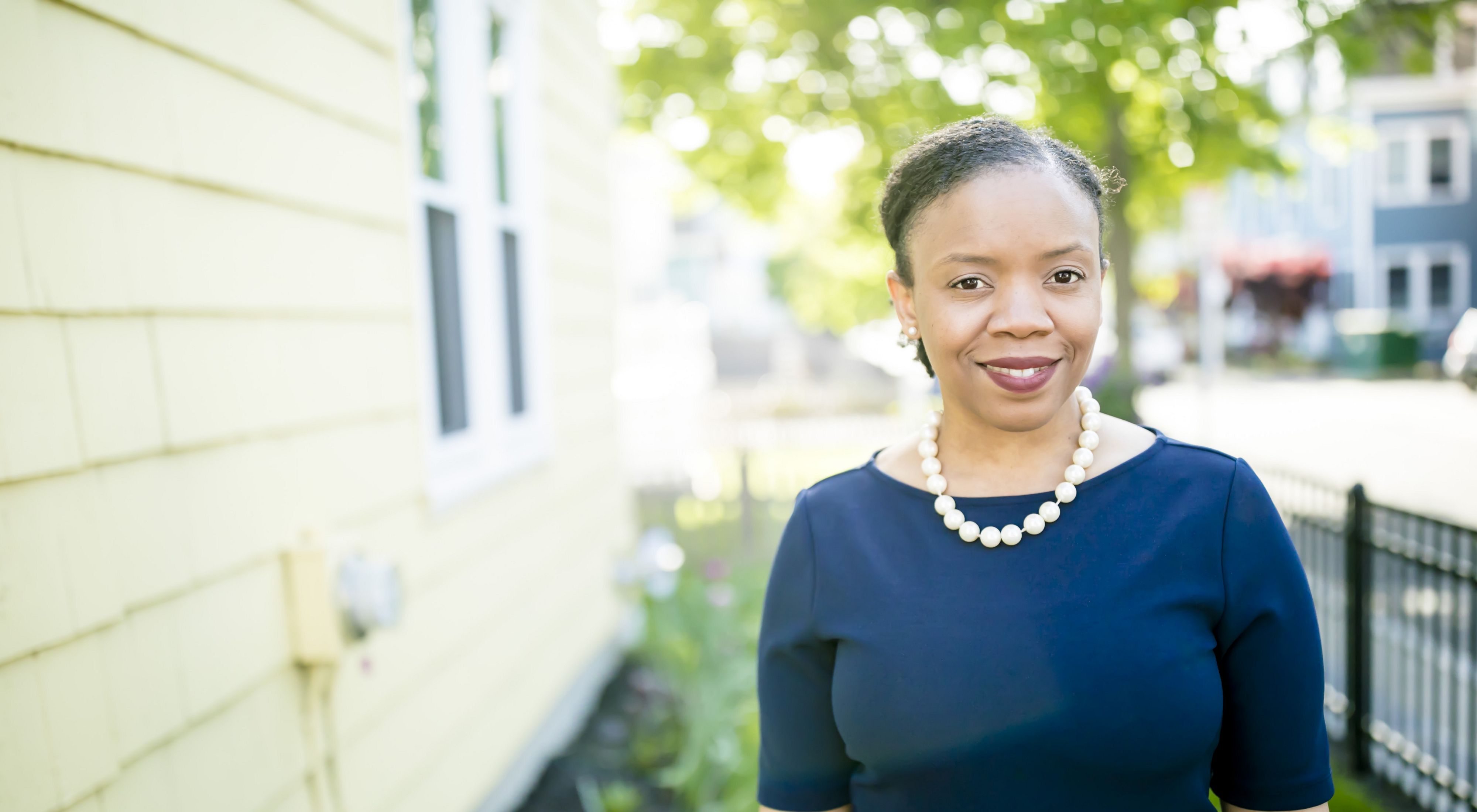 Headshot of Manikka Bowman standing in the yard of a house in a neighborhood smiling