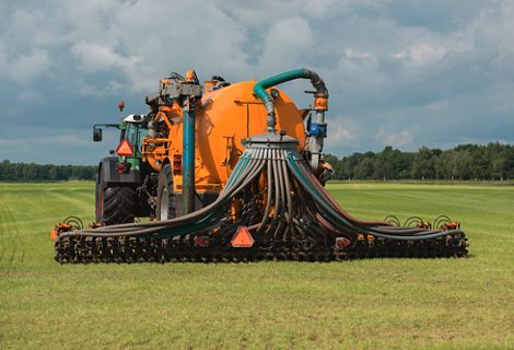A green tractor and yellow vulture spreader trailer move along a green field injecting of liquid manure.