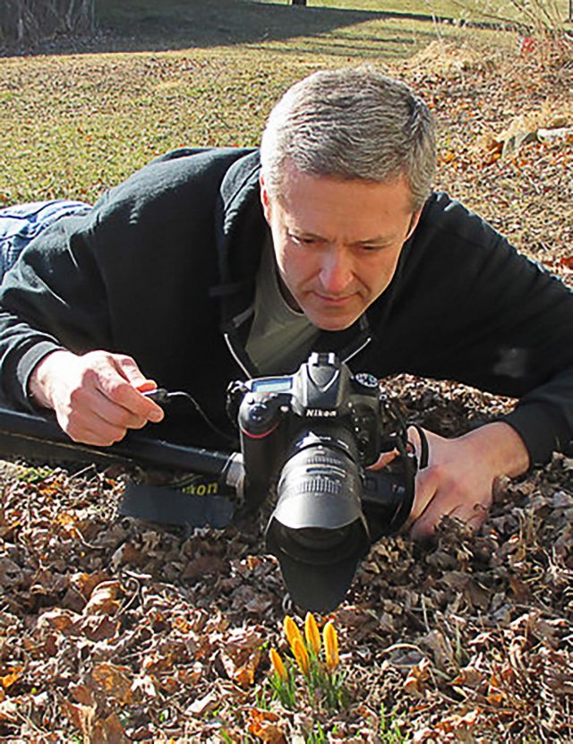 TNC staffperson Matt Williams lying on ground and focusing his camera on flower.