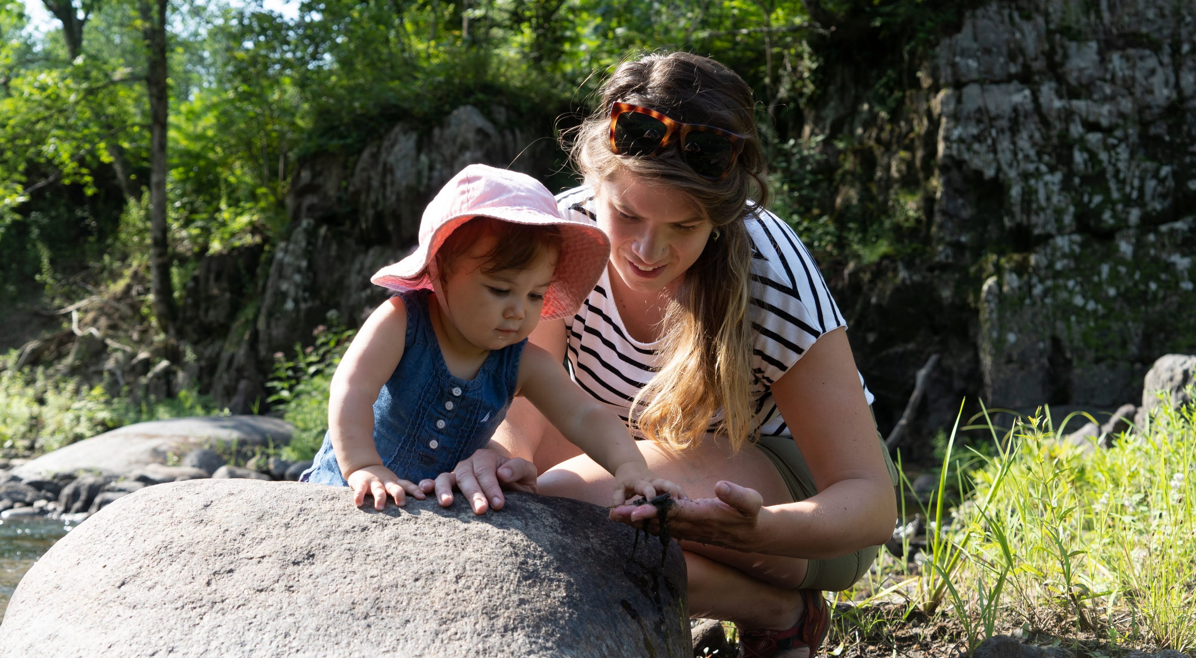 Una científica de TNC le enseña a su joven hija a inspeccionar rocas a la orilla del río.