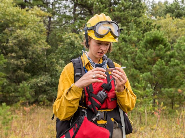 Birch Malotky uses an instrument to calculate relative humidity during a controlled burn at Kennebunk Plains Preserve.