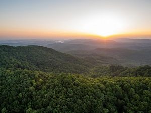 Expansive view of the sun setting over the Kentucky Appalachian Mountain region with a river running through a valley in the distance.