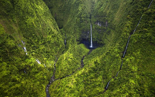 Aerial view of tall, thin waterfalls running down steep green cliffs at Wainiha Preserve in Kaua'i.