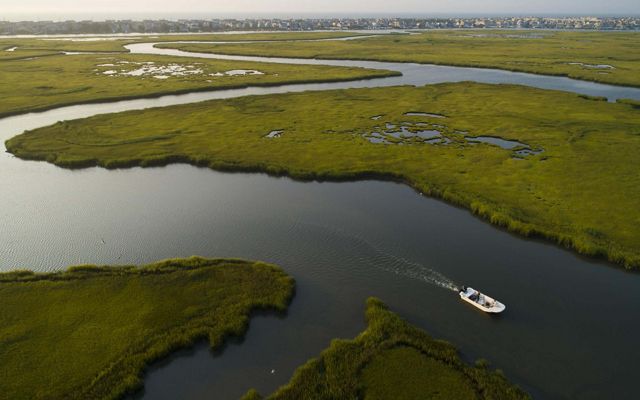 An aerial view of wetlands with a small boat navigating between them.