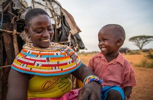 A mom and son smile at each other as she puts on his shoes.