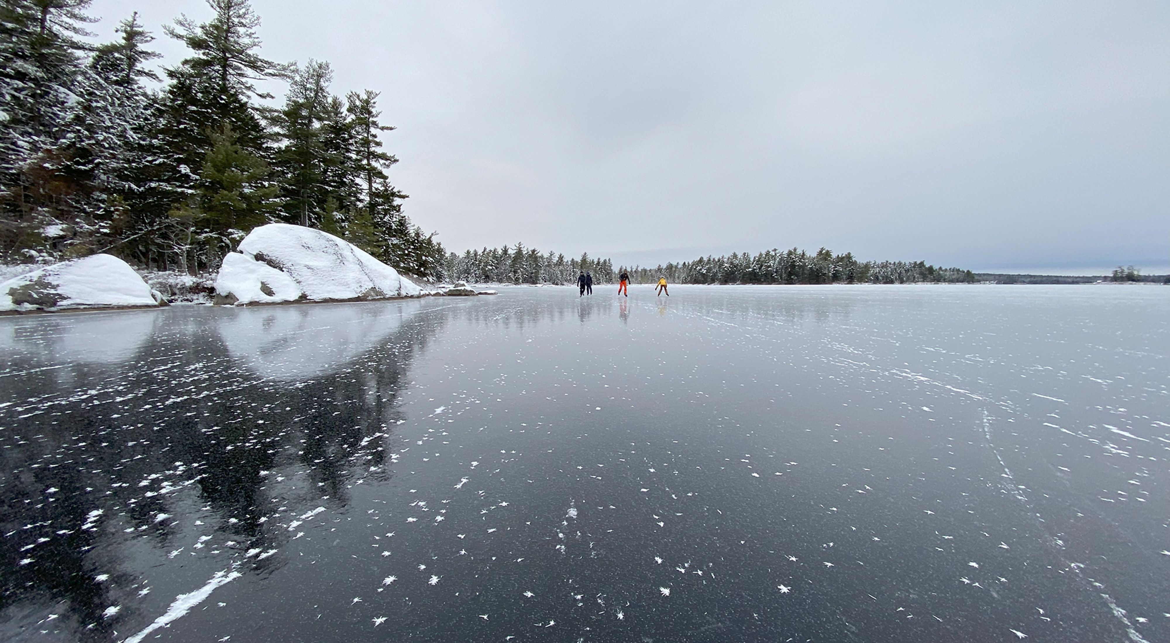People skating on a frozen lake with surrounding snow-covered forest.