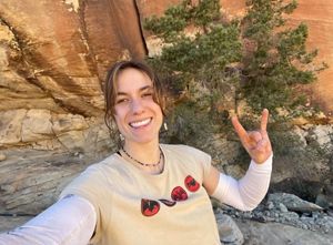 A woman smiles and makes the "rock on" sign with her hand atop a rock formation.