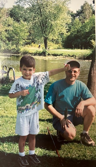 Young boy stands proudly with fishing line and fish next to father.