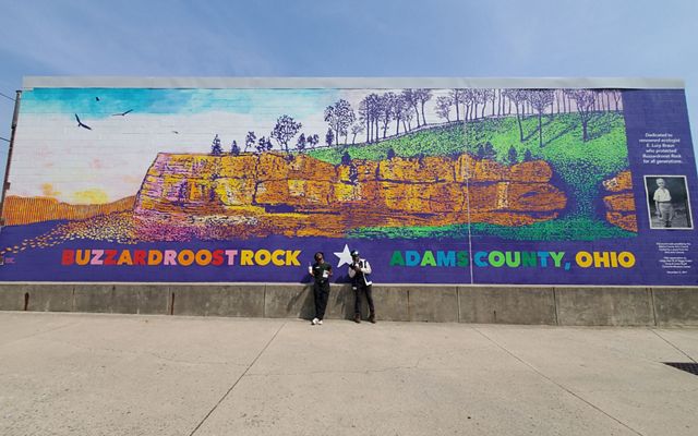 Two Groundwork ORV Green Team members stand in front of large Buzzardroost Rock mural.