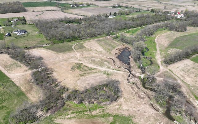 Aerial view of newly constructed stream bed winding through patches of forest.