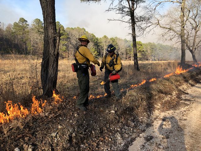 Two men exchanging equipment during a controlled burn.