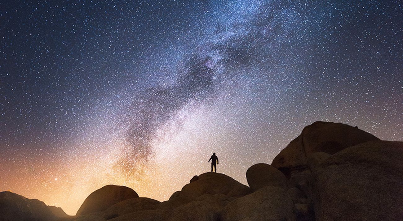 A hiker stands on a hill on a starry night.