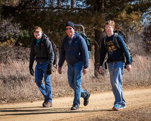 Three people wearing backpacks walk down a dirt trail.