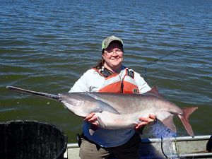 A woman in a ballcap and lifejacket holding a paddlefish on a boat in the water.