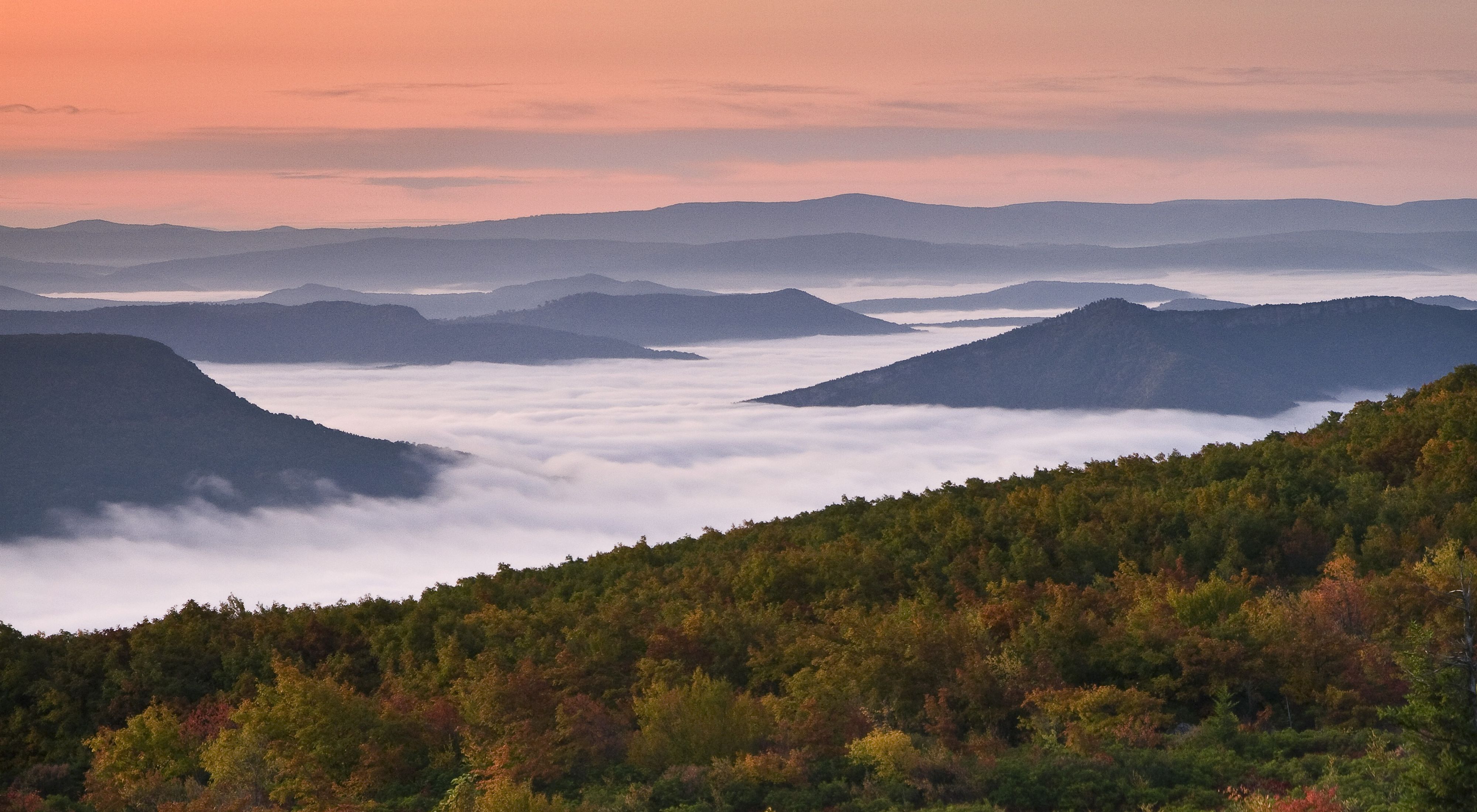 A view of misty mountain tops against an orange-and-pink sky.