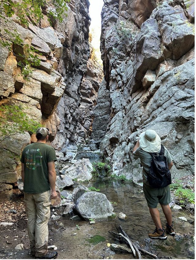 Two people stand in a narrow, rocky area while looking above.
