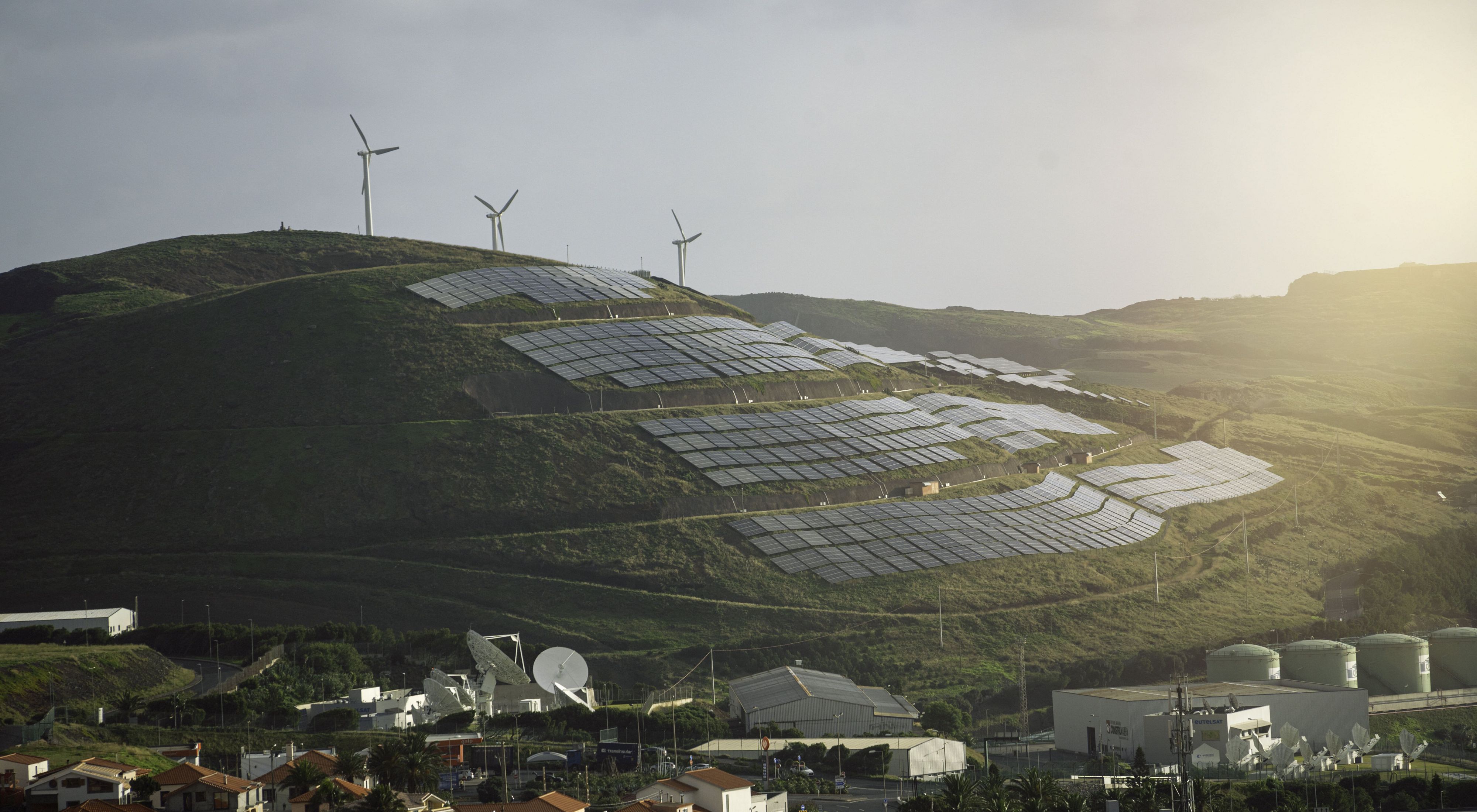 Wind turbines and solar panels on a hill above a town in Portugal in the setting sun