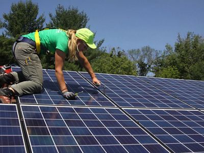 A worker kneels on a roof installing solar panels.