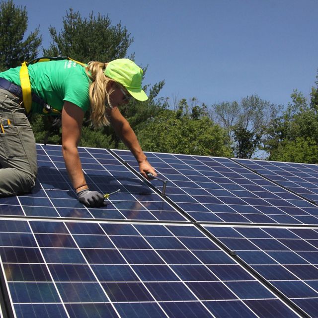 Photo of a woman installing rooftop solar panels.