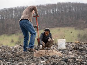 Two men work in rocks with a shovel to gather samples.