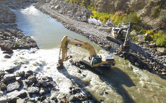 An aerial view of a construction crane picking up boulders in a river.