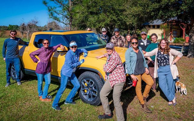 A yellow Rivian truck at Disney Wilderness Preserve is surrounded by TNC staff with smiles.