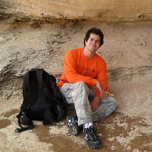 Russell Kallstrom sits on a rock with a black backpack at his feet.