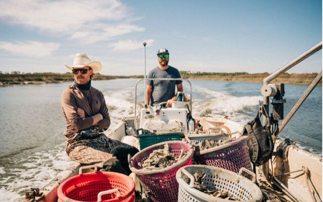 Two oystermen on a boat filled with oyster cages, on the water.