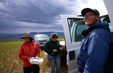 Three crew members, including Colton Folts, stand next to pickup trucks in the sage in Montana.