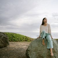 Portrait of woman sitting on a large boulder by seaside.