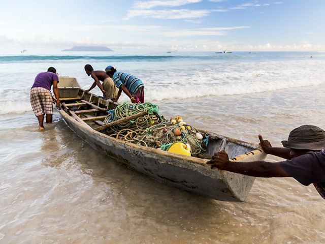 Fishermen in the Seychelles push a boat into the water