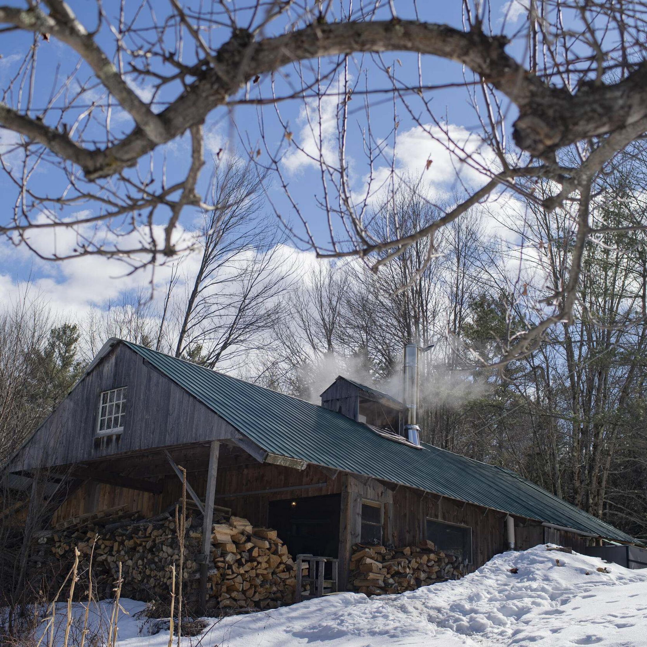 Cain in the winter with smoke coming out, snow on the ground, and wooden logs in the front. 