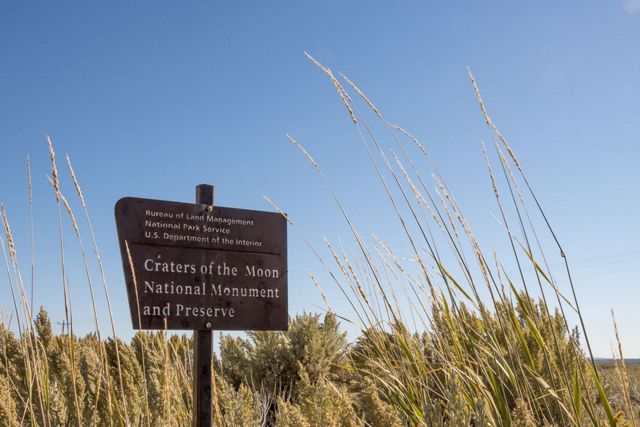 A sign for Craters of the Moon Preserve stands amidst tall golden grasses.