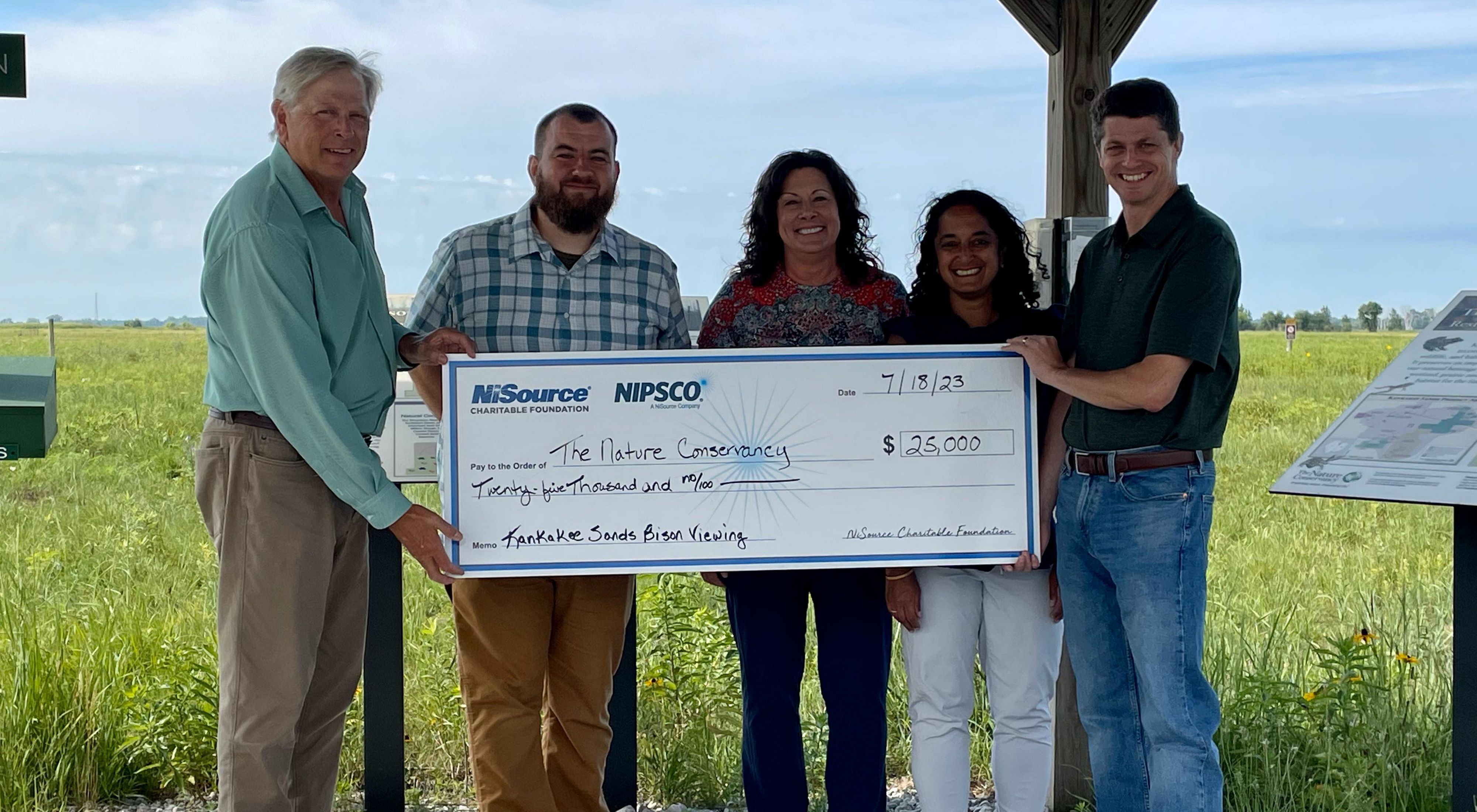 Staff from The Nature Conservancy and NiSource/NIPSCO stand under a wooden structure at Kankakee Sands and hold an oversized check made out for $25,000.