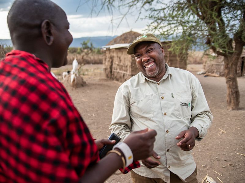 Two men smile and laugh as they talk together in a traditional Maasai village.