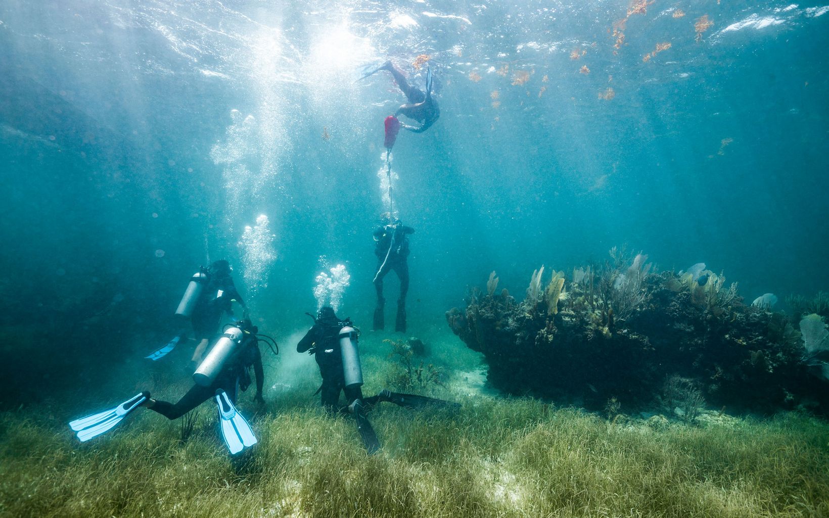 Five divers practice inflating a lift bag underwater near Puerto Morelos, Mexico.